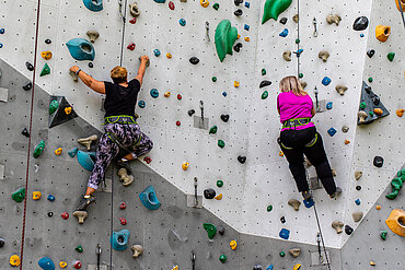 Auf dem Bild sieht man zwei Personen die an einer Kletterwand klettern.