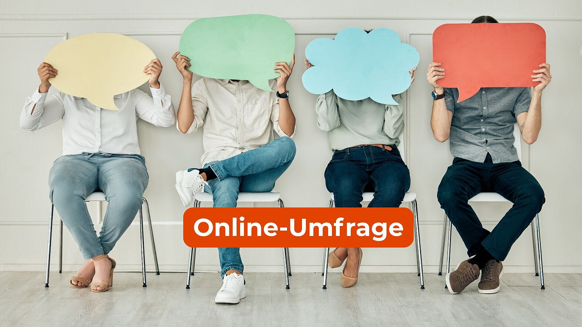 Vier Menschen auf Stühlen, die Sprechblasen aus Papier vor ihr Gesicht halten.