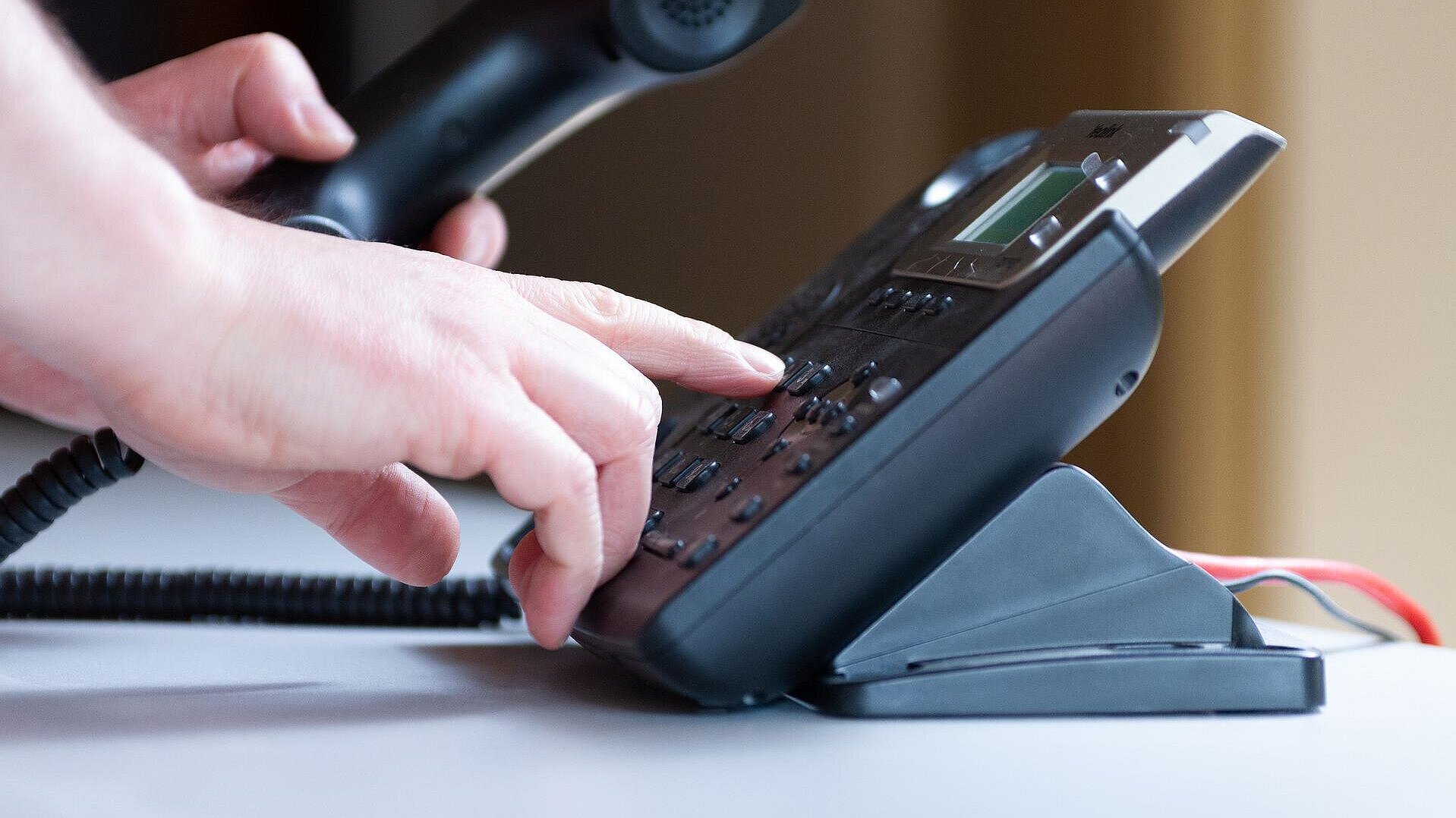 Eine Hand an einem Bürotelefon.